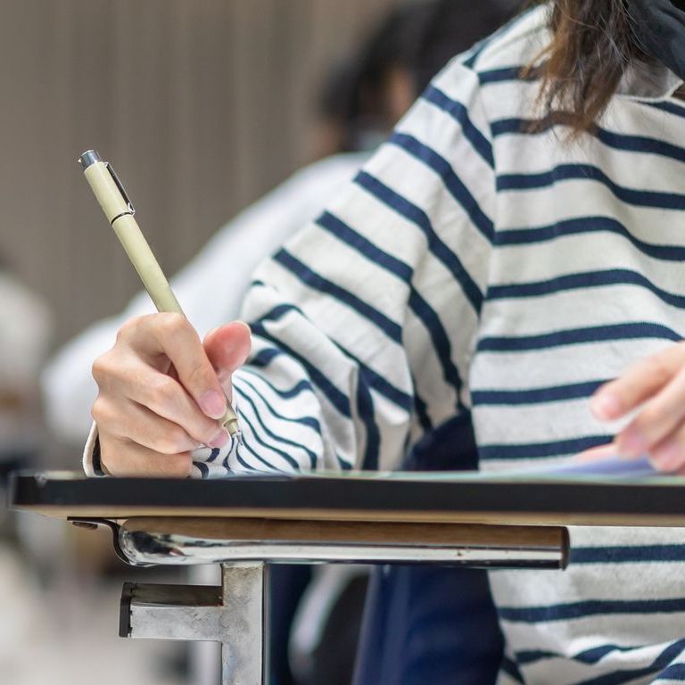 A woman in a striped shirt is writing on a piece of paper with a pen.