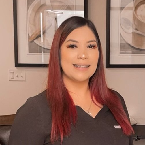 Woman with dark hair and red highlights wearing a black top, smiling with braces.