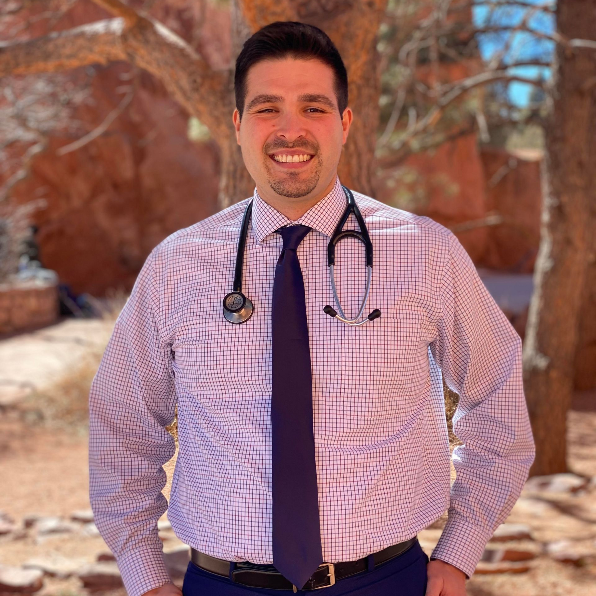 Man in a maroon button-down shirt smiles, standing against an outdoor scene.