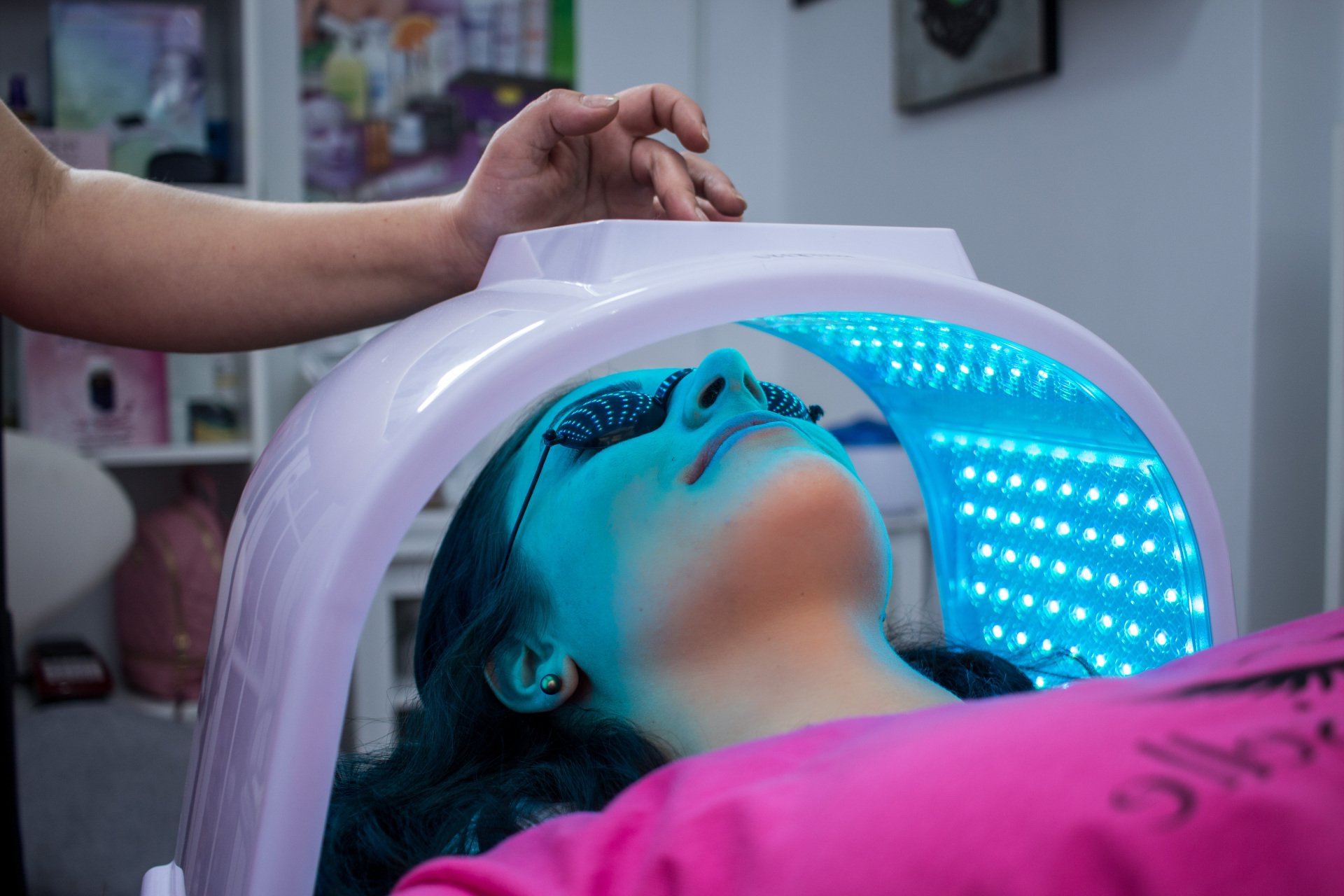 Woman undergoing LED light therapy at a spa, wearing protective eyewear under a blue light treatment.