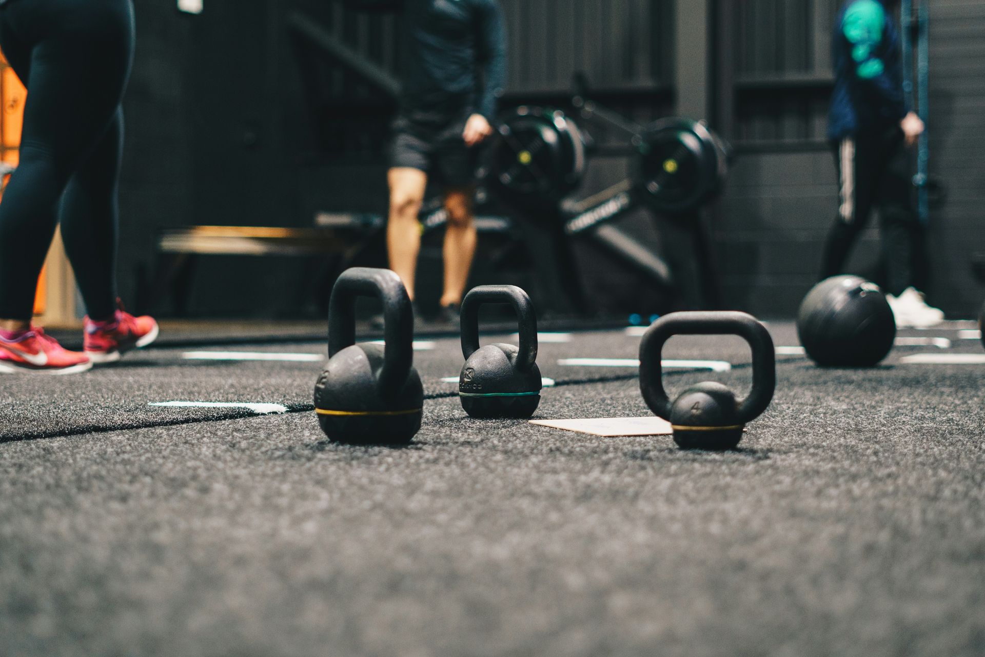 Kettlebells on gym floor with people working out in background.