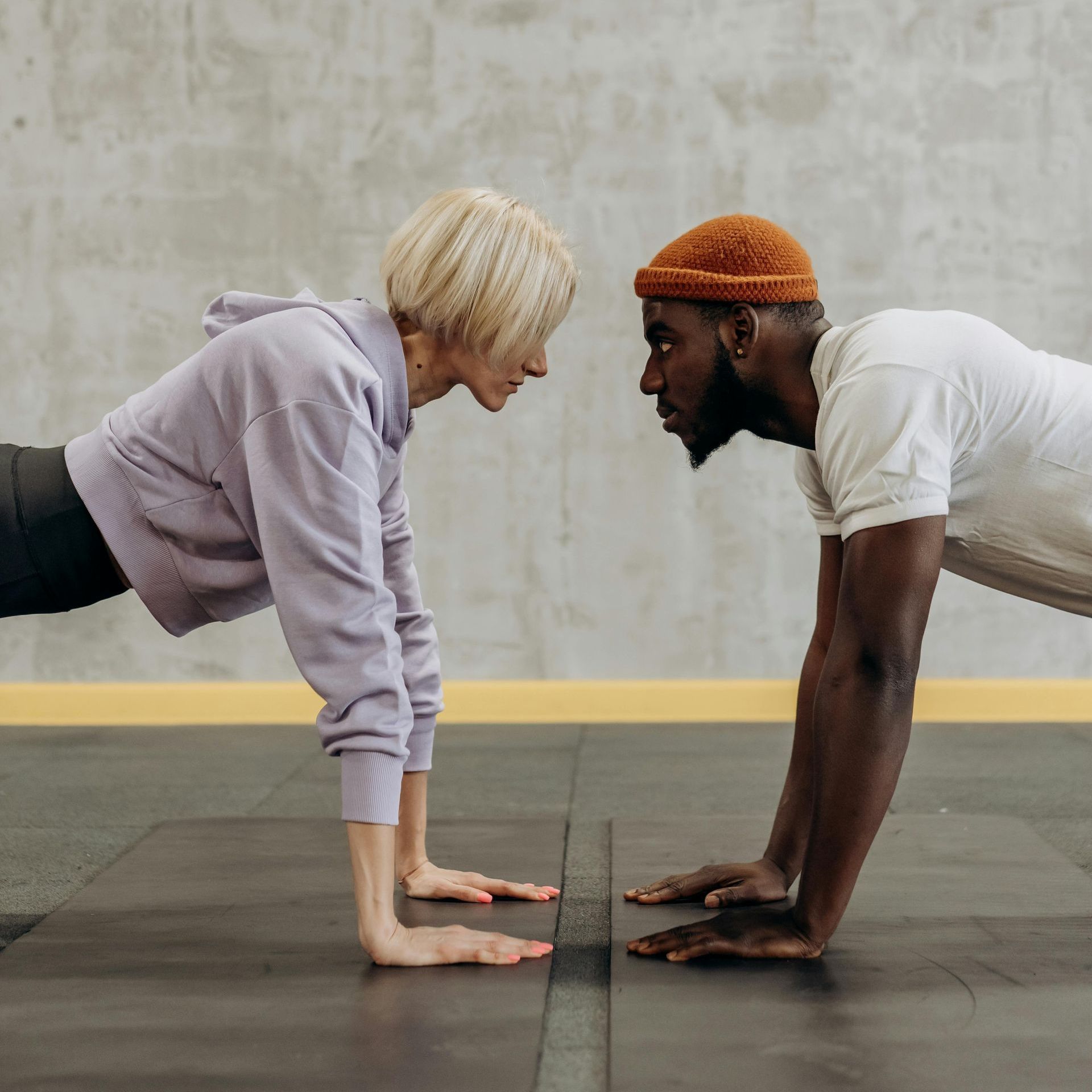 A woman and a man, facing each other, doing push-ups. Both have serious expressions on their faces.
