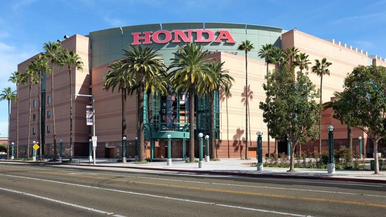 Honda Center building with red Honda sign; tall palm trees in front on a sunny day.