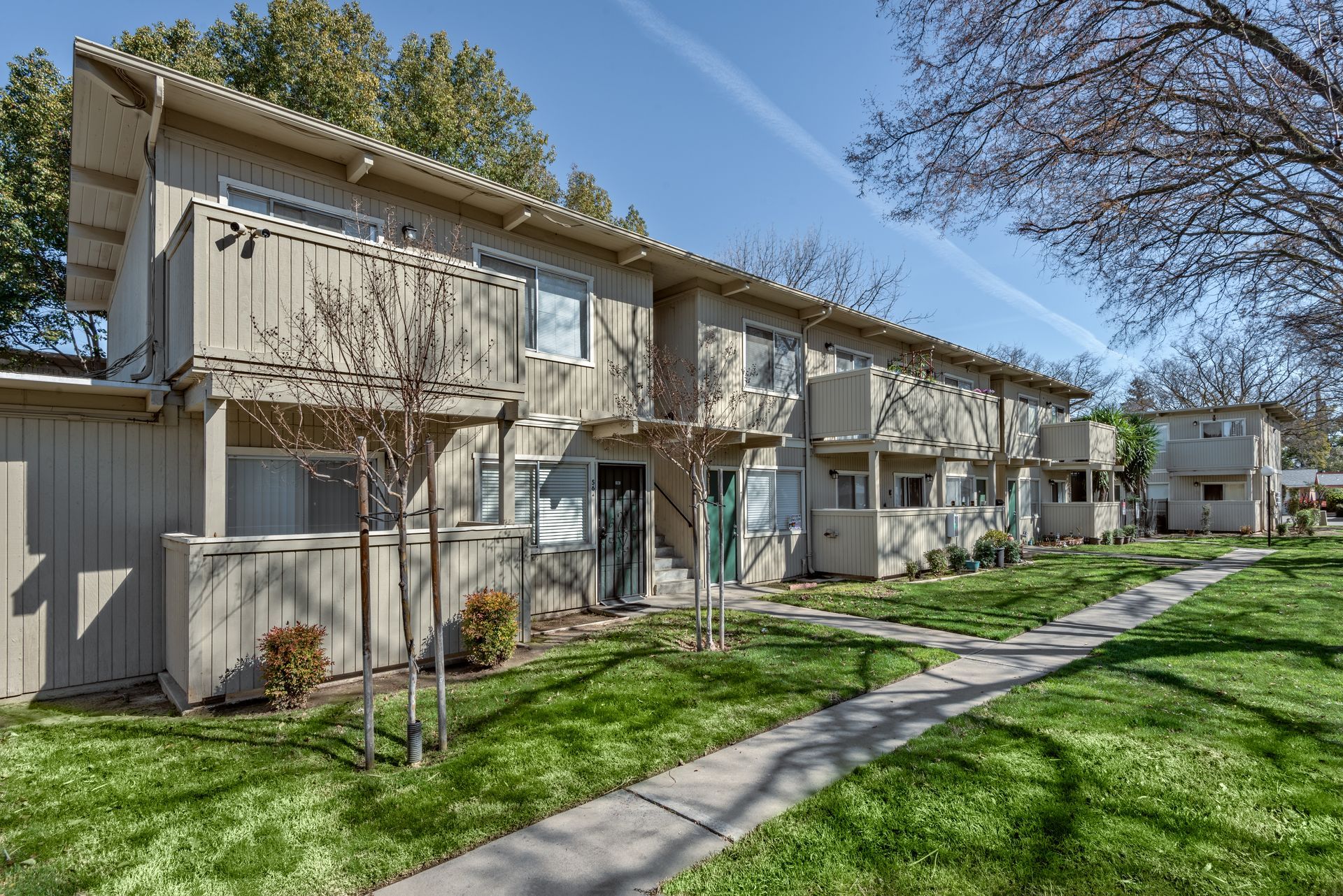 A row of two-story townhouses with beige siding and green lawns on a sunny day.