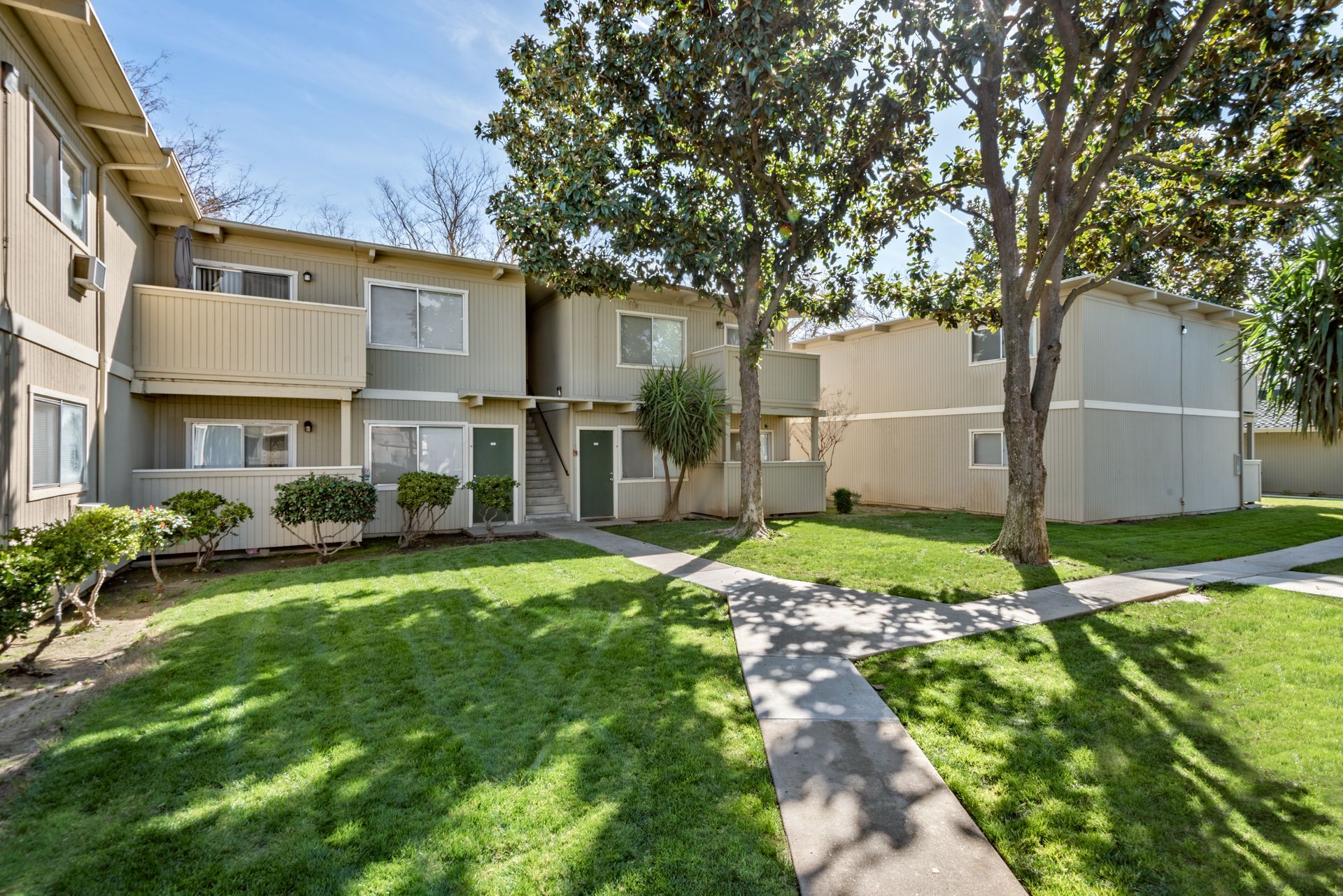 Two-story beige apartment buildings with green lawns and trees in front.