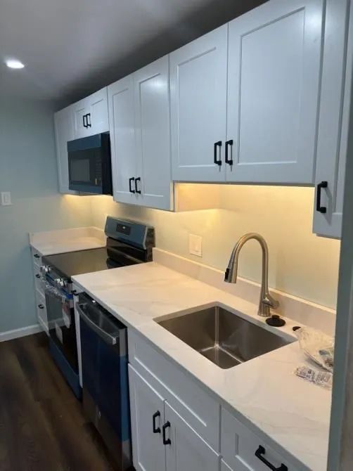 A modern kitchen featuring white cabinets with black hardware, a stainless steel sink, and white countertops.