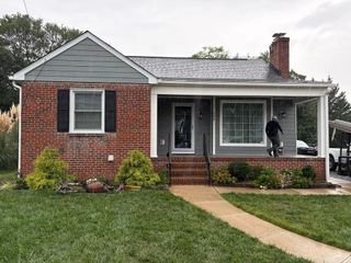 A single-story brick house with a gray gable, covered front porch, and a person walking toward the entrance.