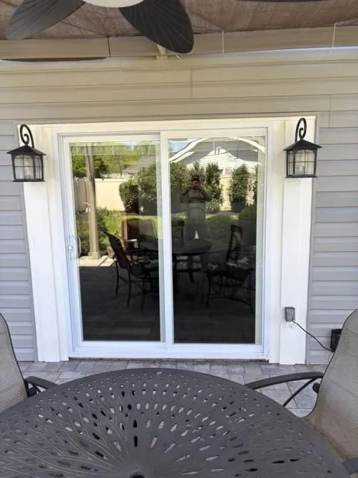 A sliding glass door on a house exterior featuring white trim, gray siding, and a decorative lamp on each side.