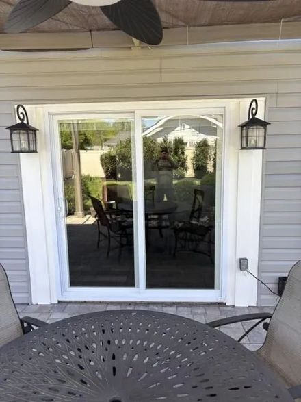 A sliding glass door on a house exterior featuring white trim, gray siding, and a decorative lamp on each side.