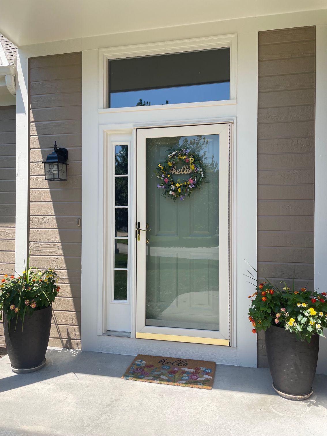 Front entry with white door, wreath, sidelights, and potted flowers on a sunny porch