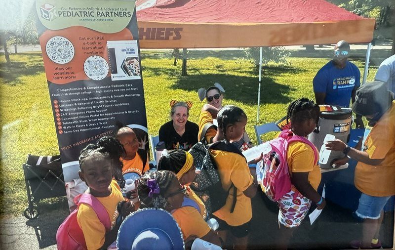 People gathered at an outdoor booth under a pink tent, with a banner and informational display.
