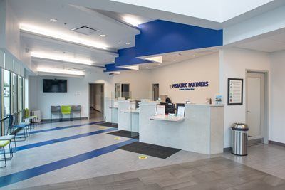 The modern reception area of Pediatric Partners, featuring a blue and white front desk, seating, and a waiting room.