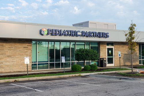 Exterior view of a Pediatric Partners office building with stone walls, large glass windows, and a parking lot.