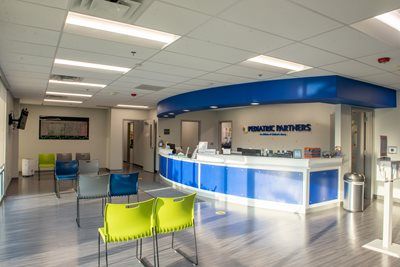 Waiting area with lime green and blue chairs in front of a blue and white Pediatric Partners reception desk.