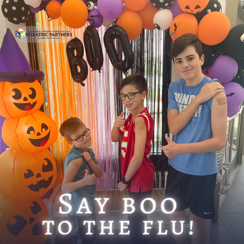 Three children posing in a Halloween-themed office after receiving flu shots, with text reading
