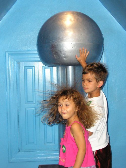 A boy touches a Van de Graaff generator while a girl with electrified, standing-up hair stands in front.