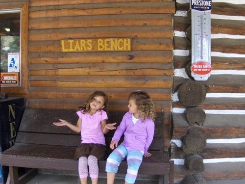 Two children sit on a wooden bench under a sign reading