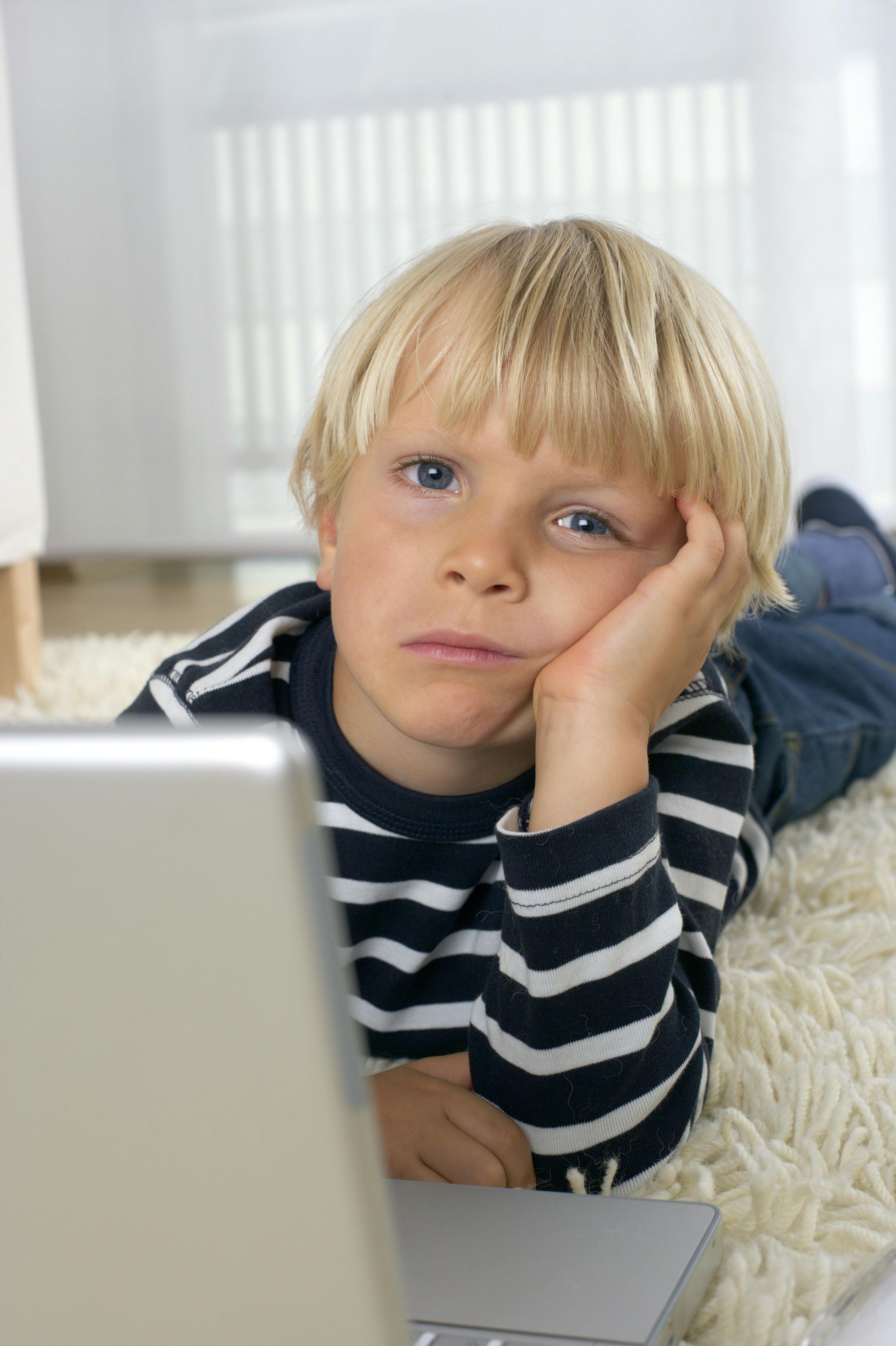 child laying on the floor with his face laying on his hand and a bored look