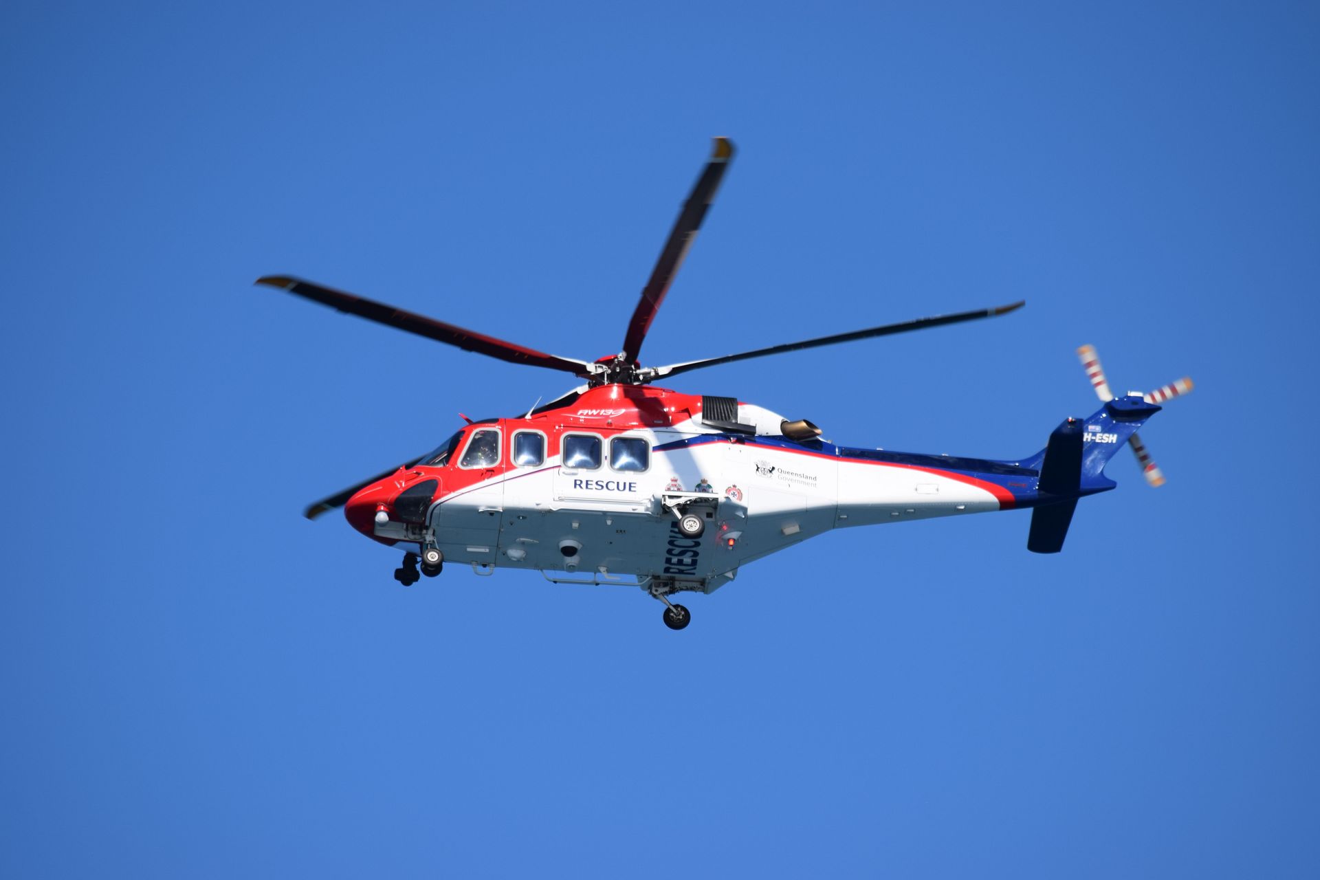 Red, white, and blue helicopter with the word RESCUE on the door flying against a clear blue sky