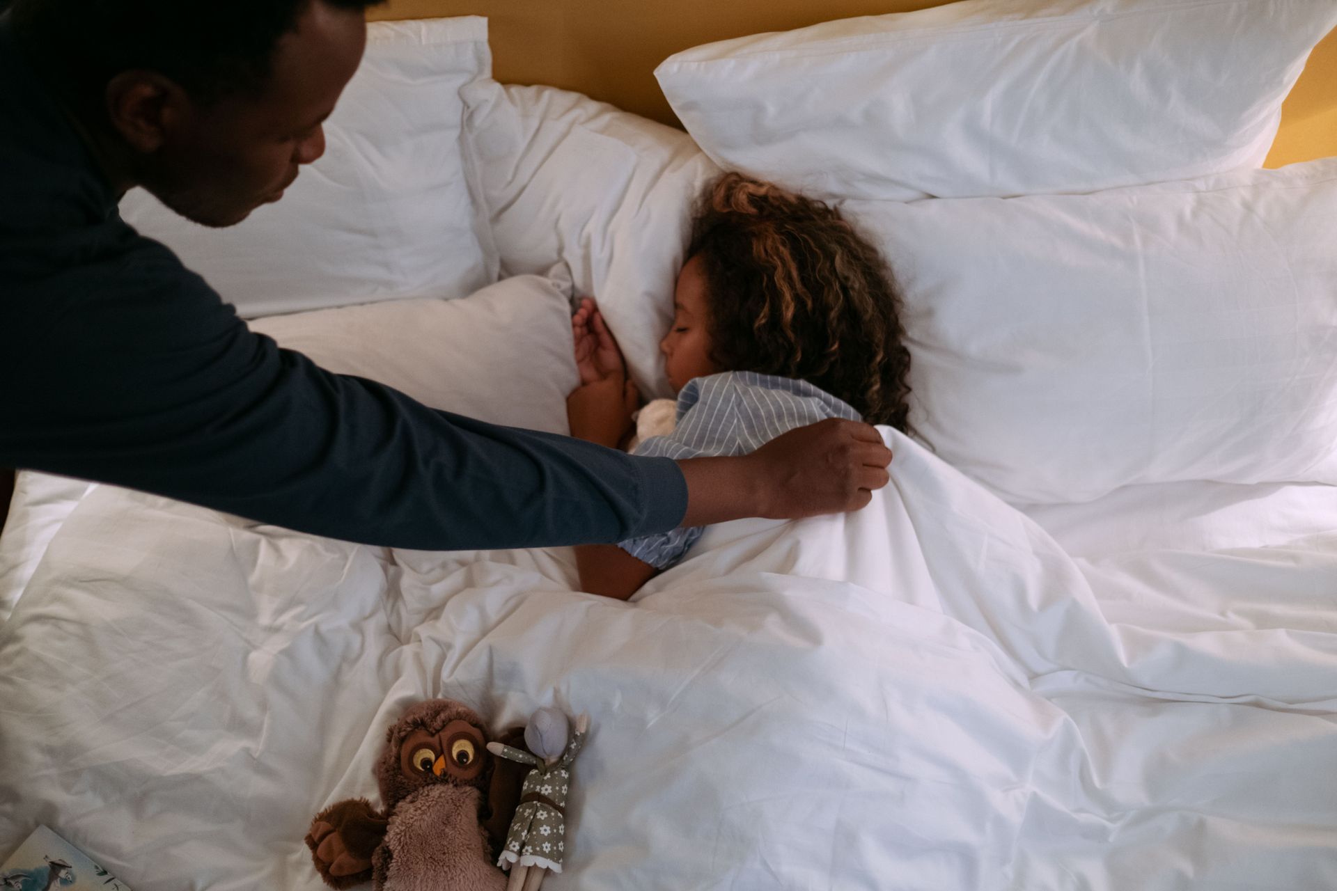Child getting tucked into bed by her father
