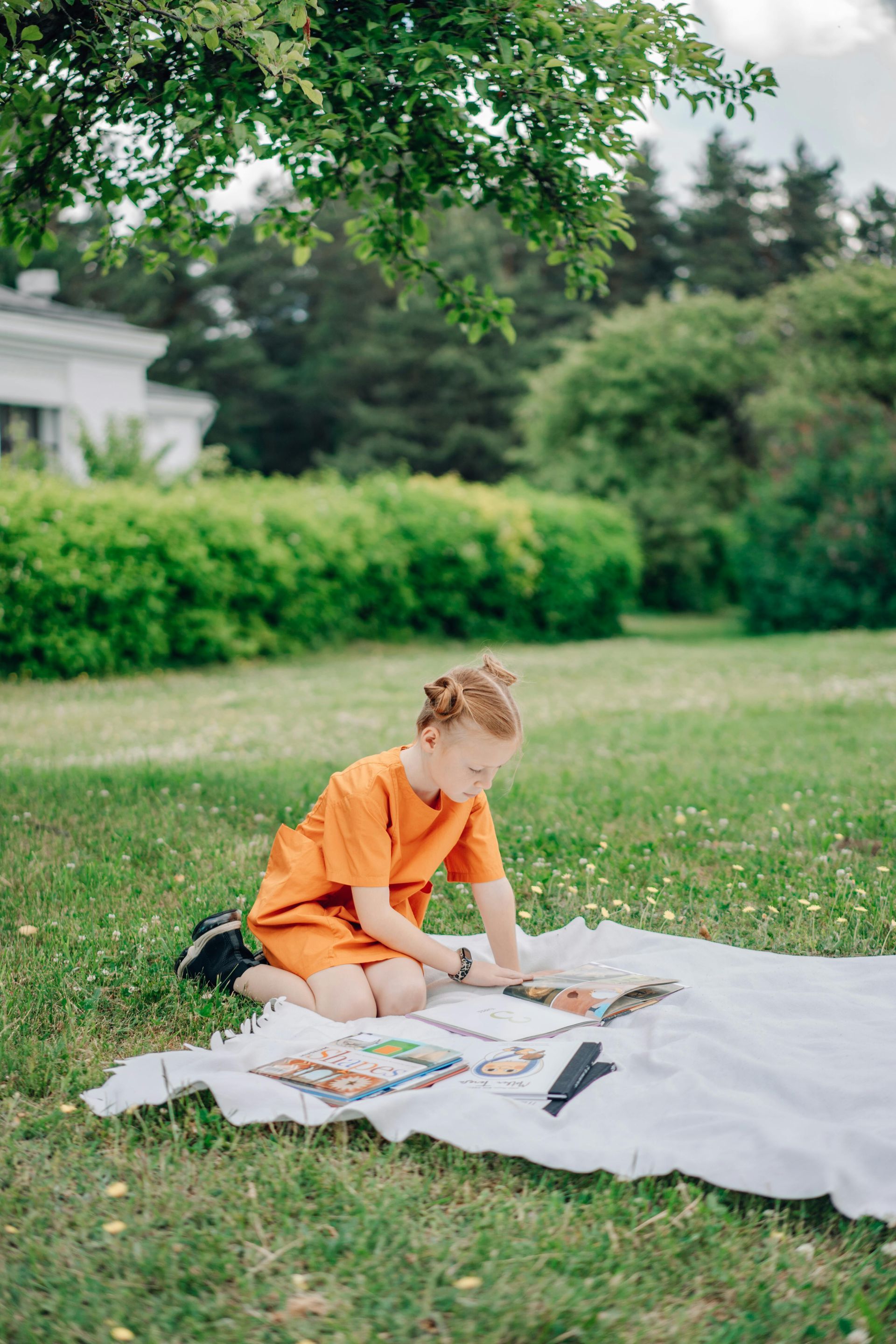 A child happily reading a book outdoors in a sunny park setting.