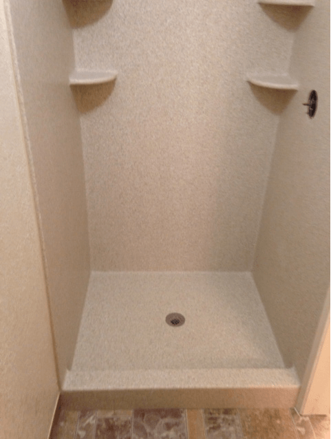 A shower stall with shelves and a hole in the floor