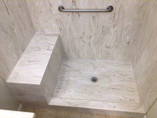 A bathroom with a walk in shower with a seat and a hand rail.