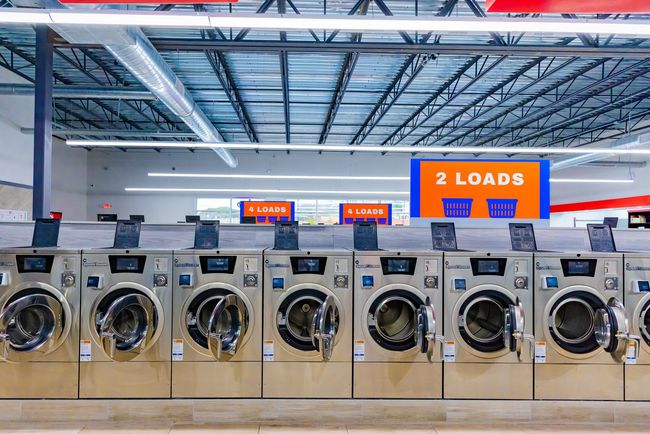 A person is jumping out of a washing machine in a laundromat.