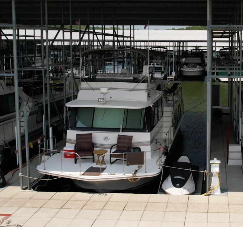 A boat is docked under a covered dock with a few chairs on the deck
