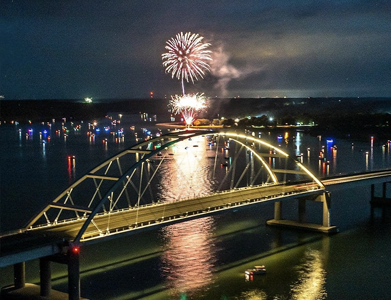 Fireworks are displayed over a bridge over a body of water