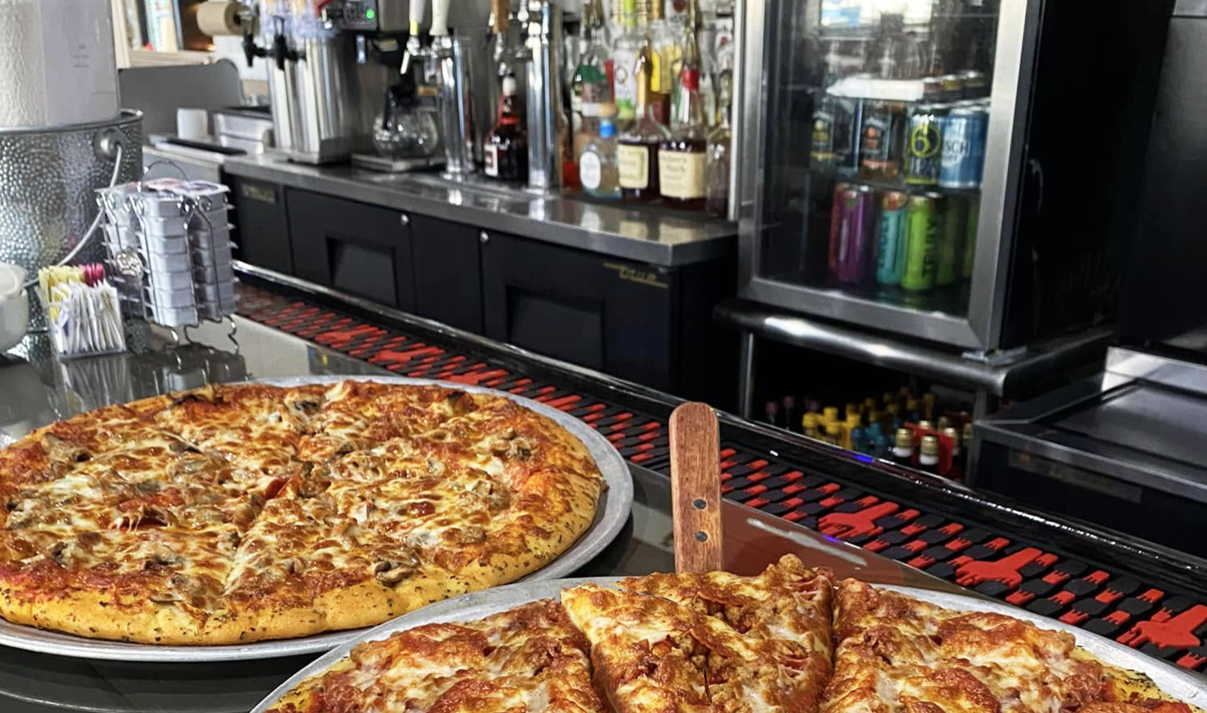 Two pizzas are sitting on a counter in a restaurant.