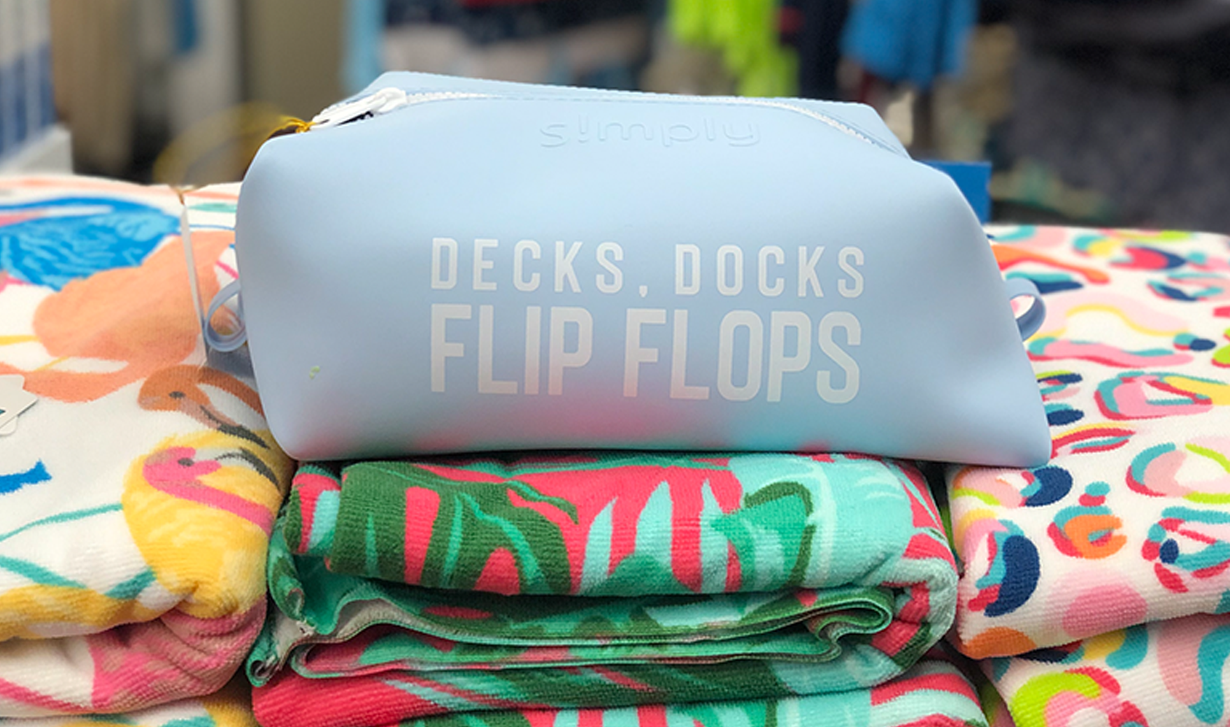 A bag that says decks , docks flip flops is sitting on top of a pile of towels.