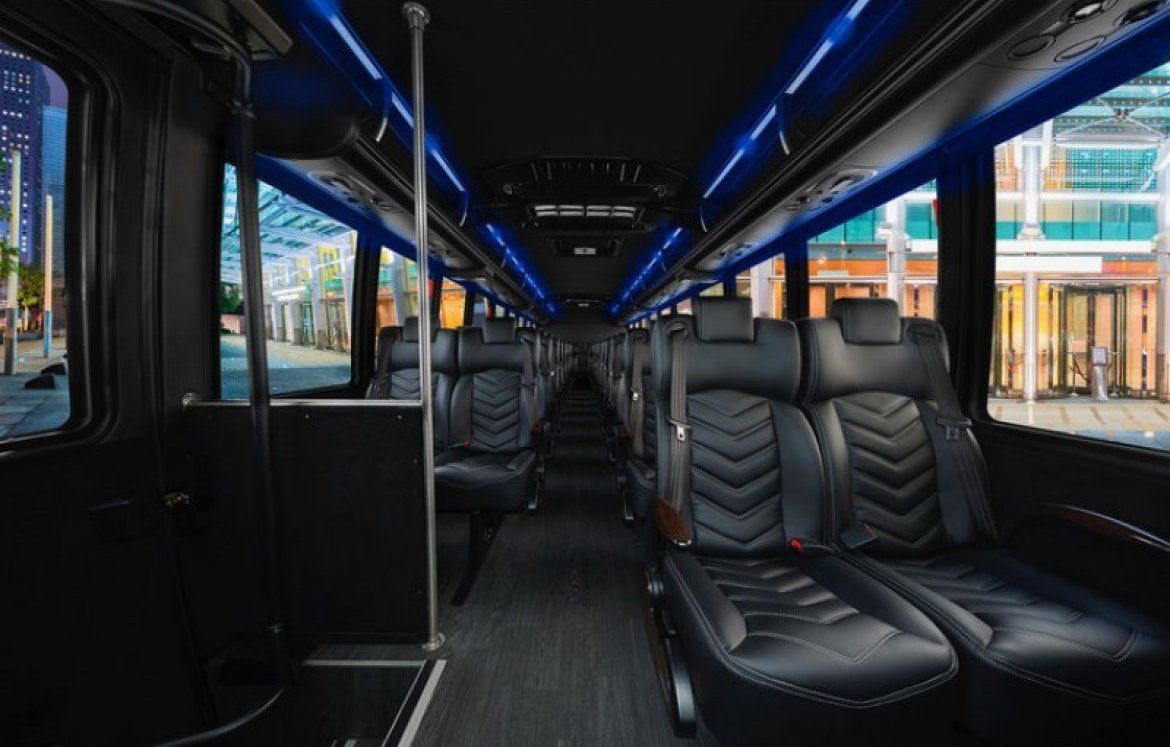 Interior of a sleek black bus with rows of seats. Blue lights shine overhead, and windows offer city views.