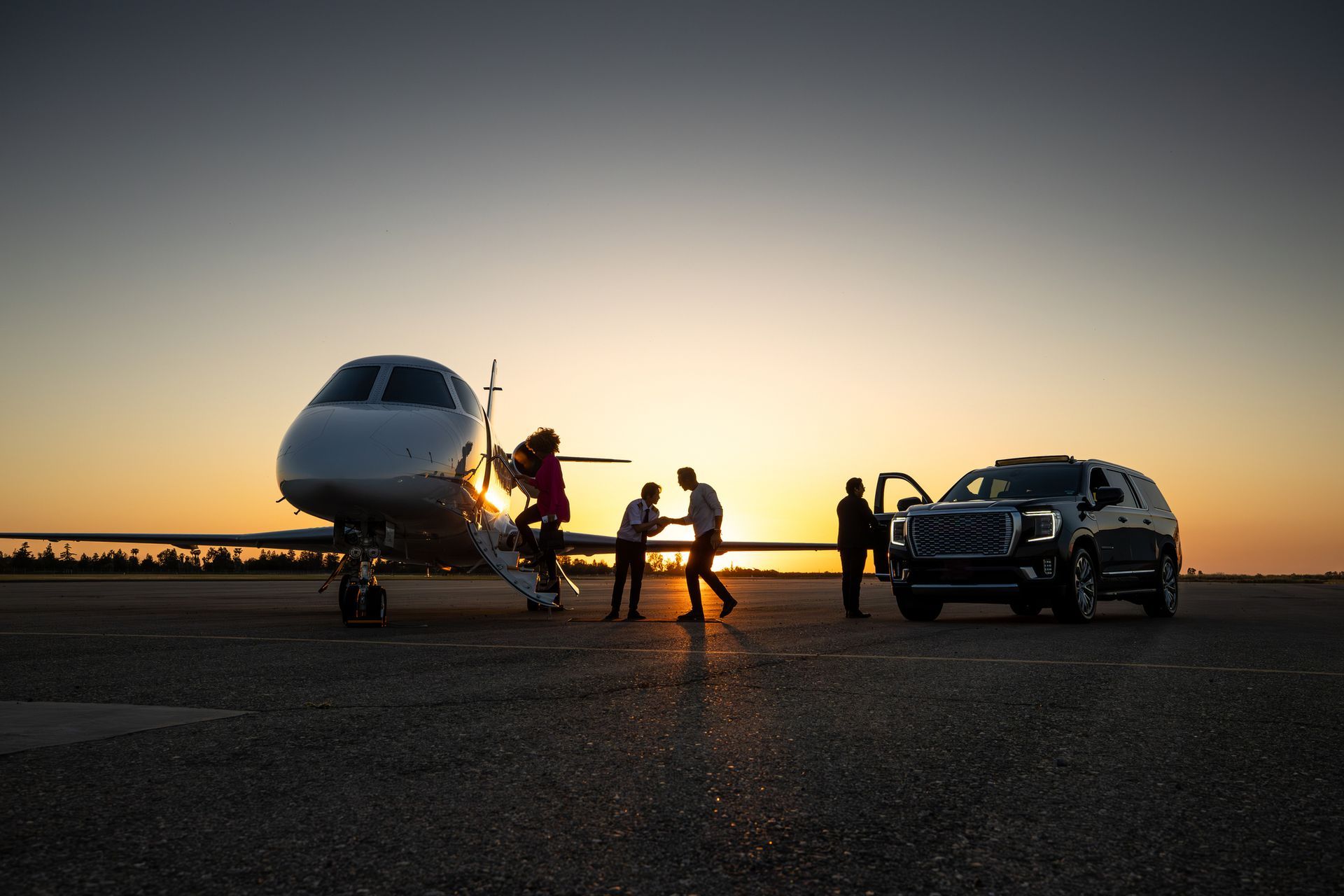 People exiting a private jet onto a tarmac, greeted by an SUV in the sunset.