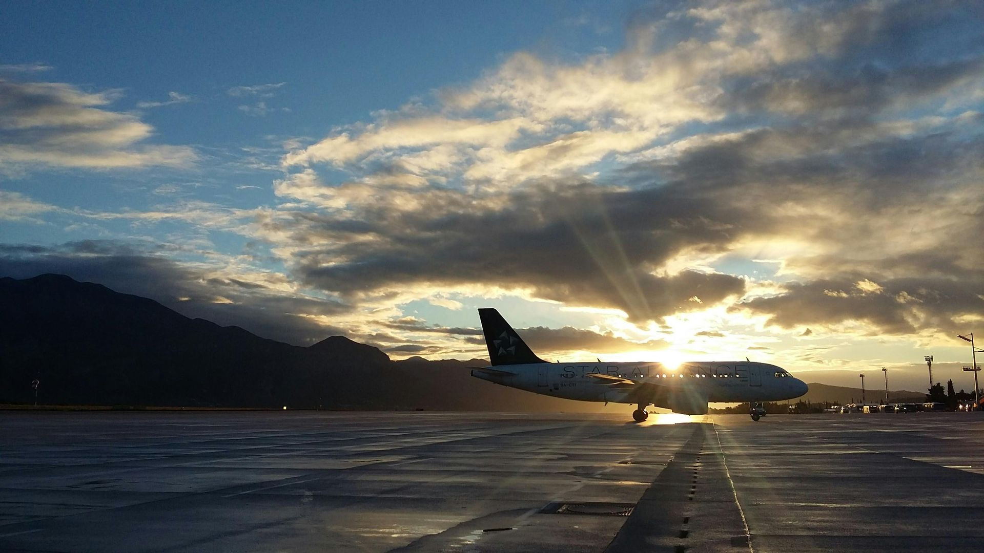 Airplane on runway at sunset; mountains in the background, dramatic sky.