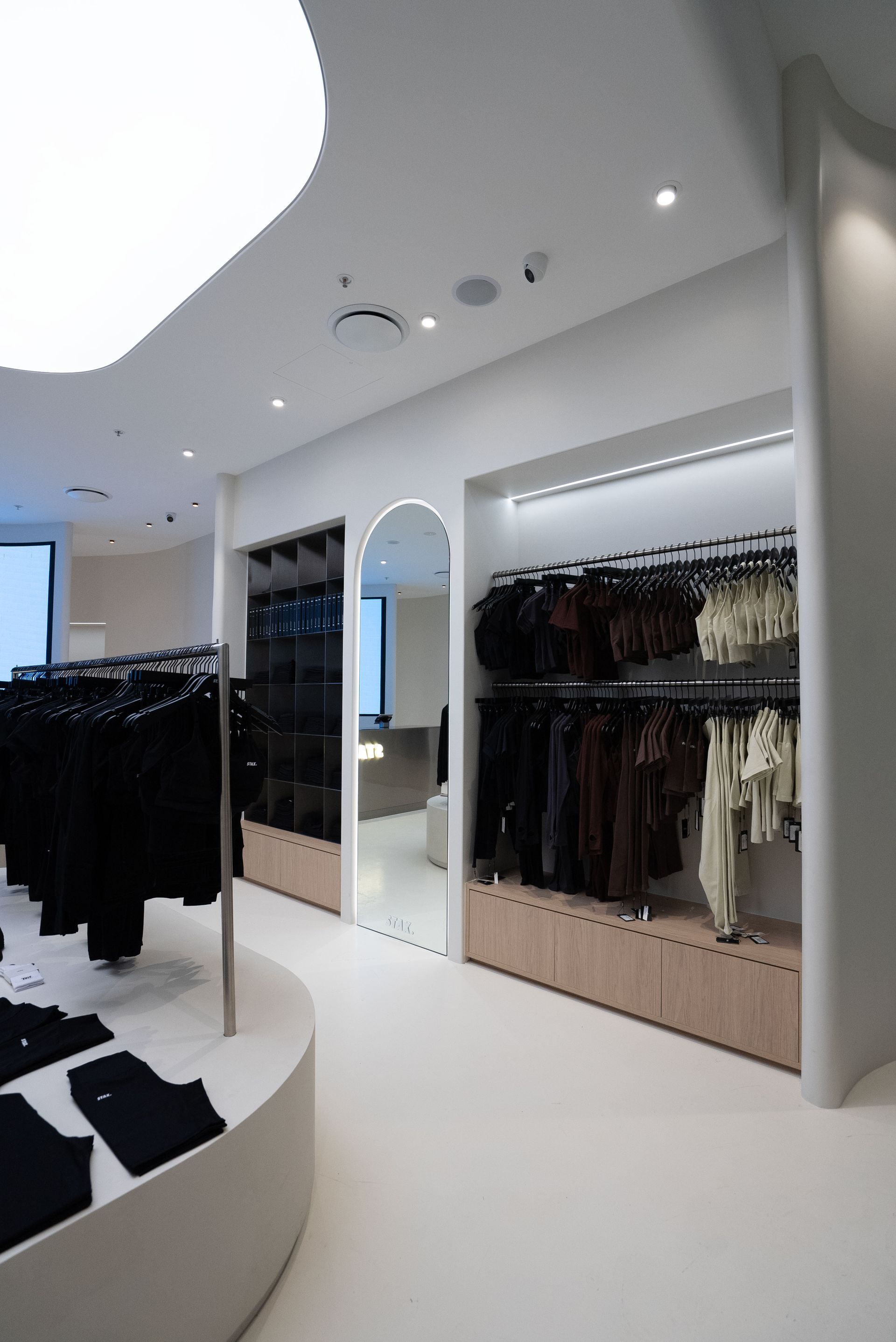 Modern clothing store interior with white walls, curved displays, and clothing racks.