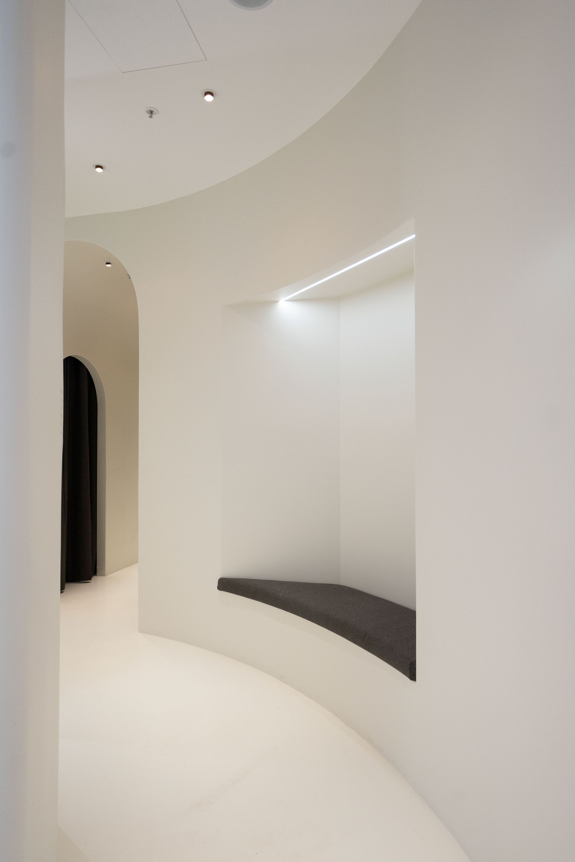 White curved hallway with built-in seating area; dark gray seat, minimalist design.