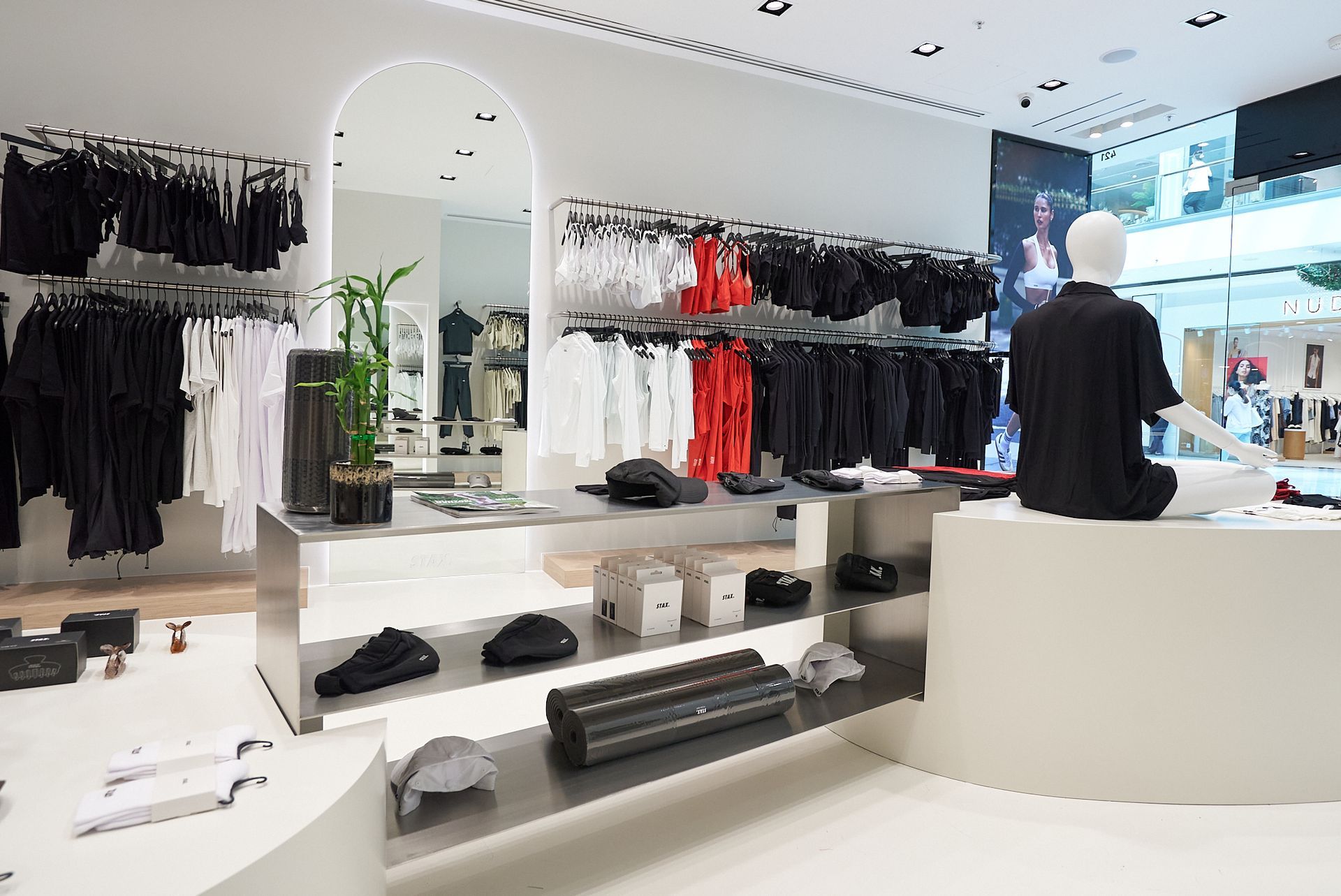 Clothing store interior with white walls, displays of apparel in black and white, and a seated mannequin.
