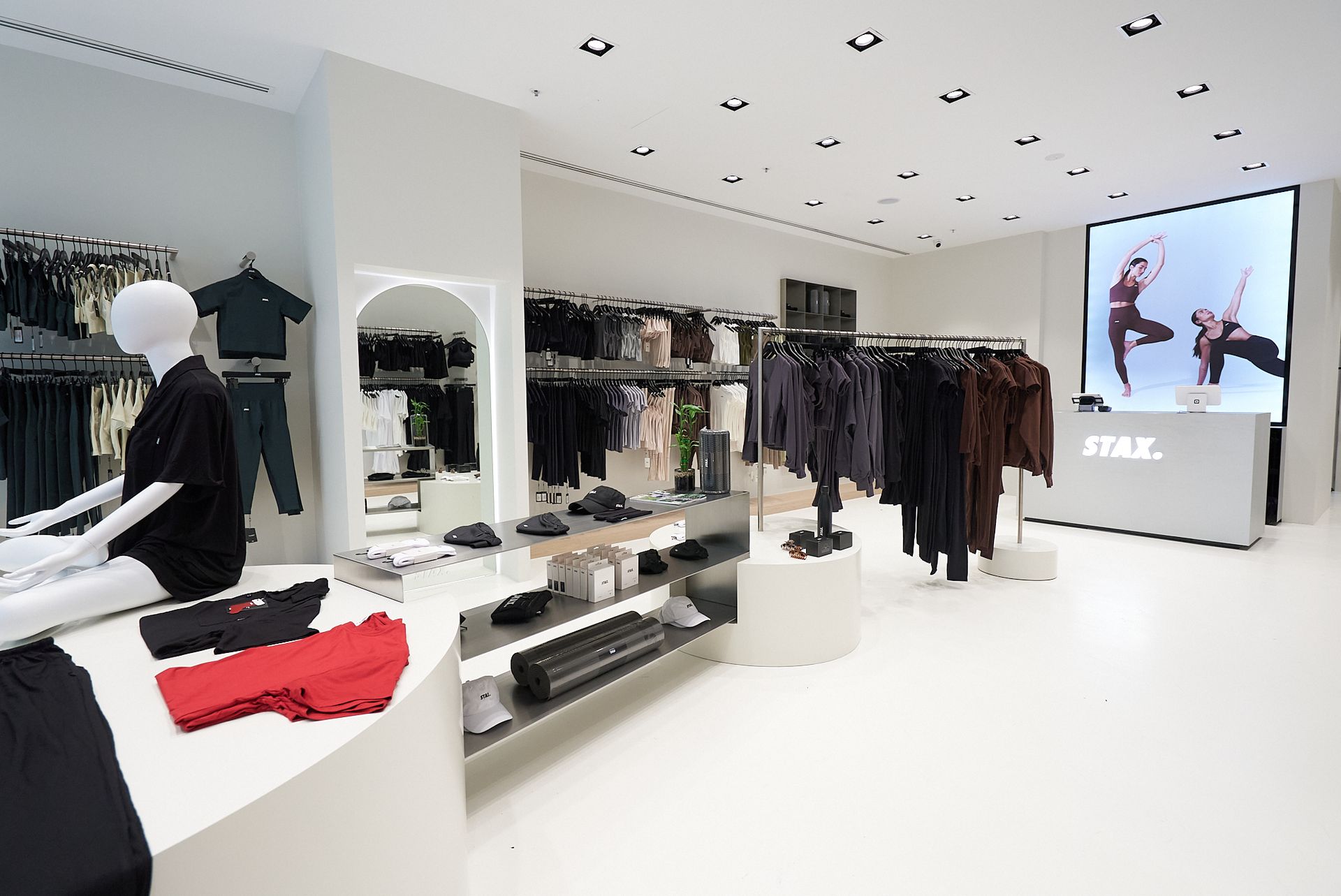 Modern clothing store interior with mannequins, racks of clothing, and video screen.