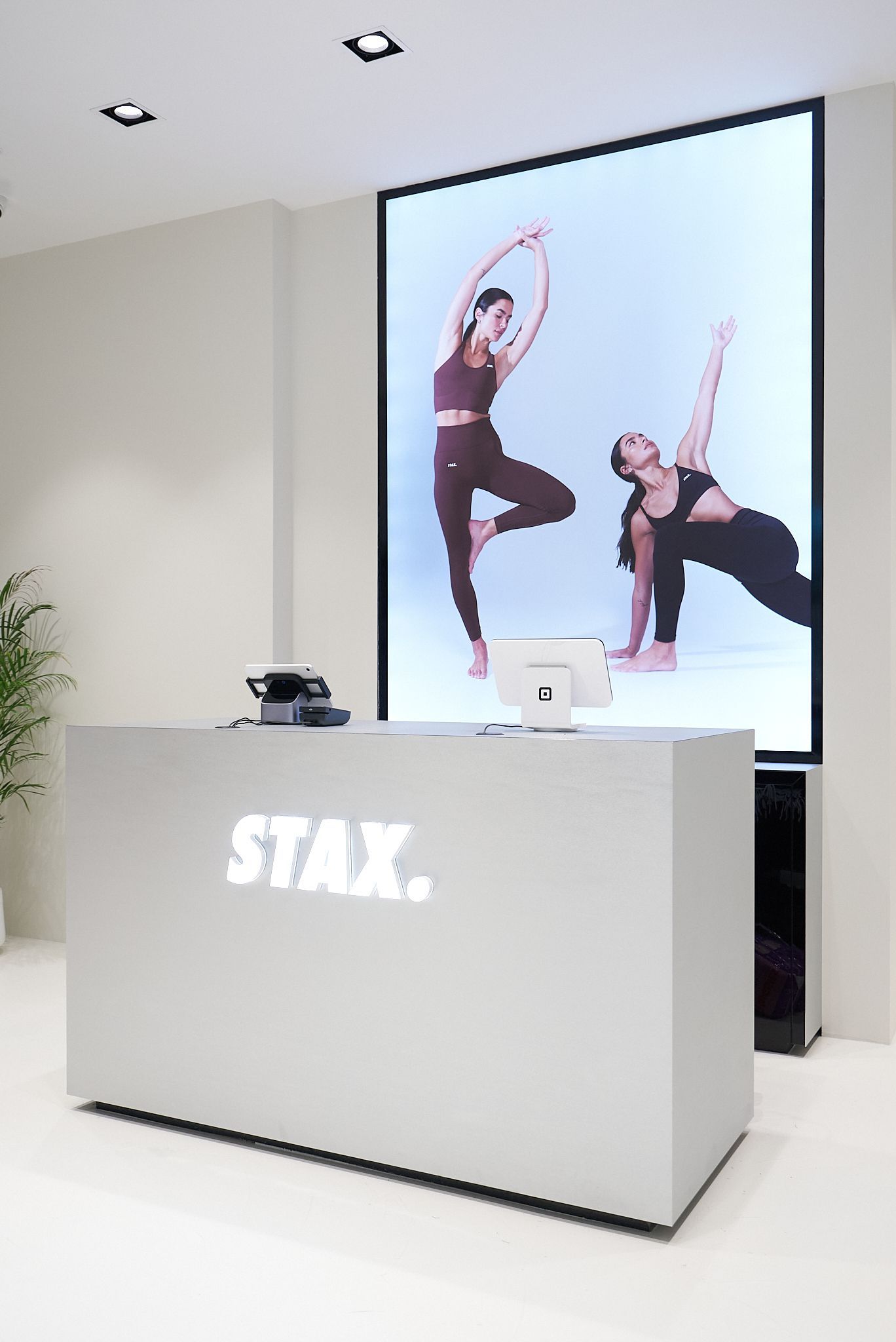 STAX. store front desk with a large screen displaying two women in workout attire.