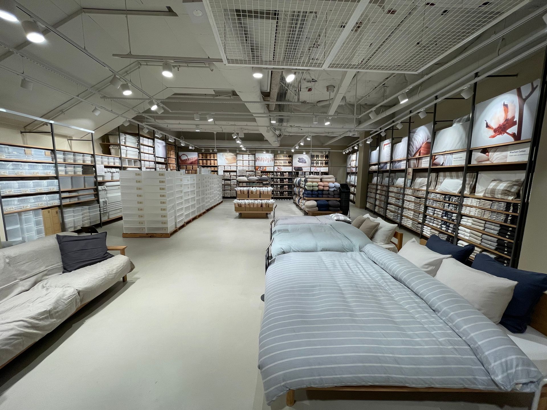 Interior of a home goods store with bedding and furniture displays. Shelves with various products are on either side.