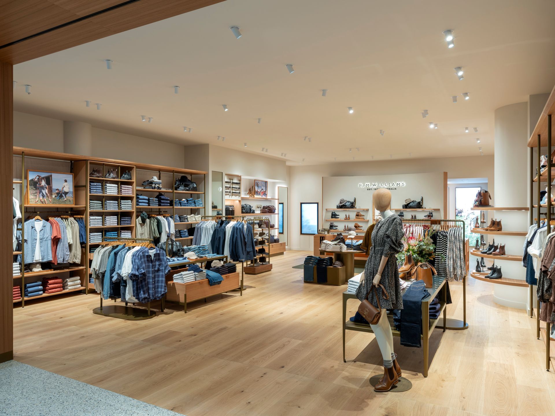 Clothing store interior with wooden shelving and display tables, displaying jeans, shirts, and accessories.