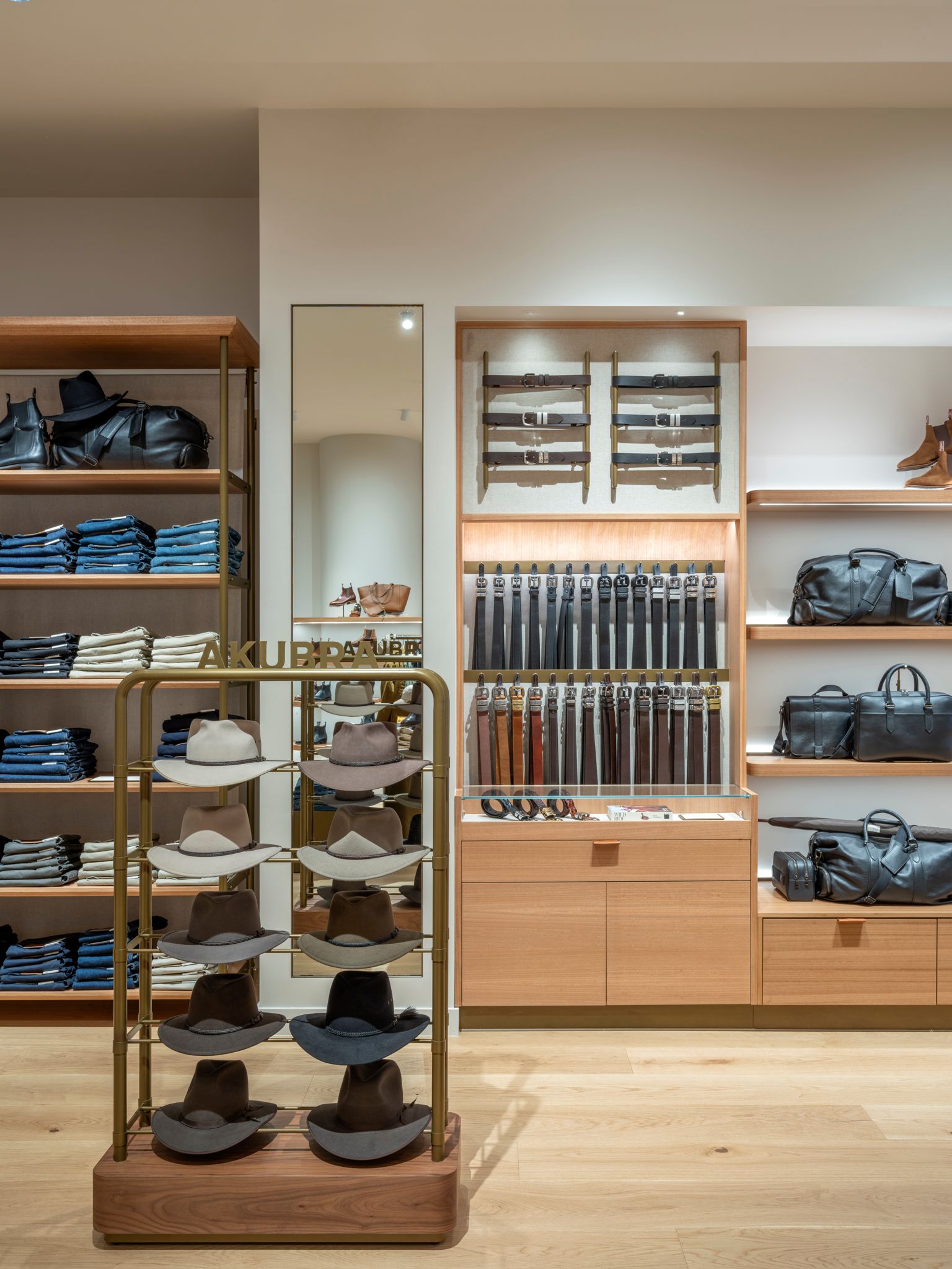 Retail display showcasing hats, belts, bags, and folded clothing on wooden shelves.