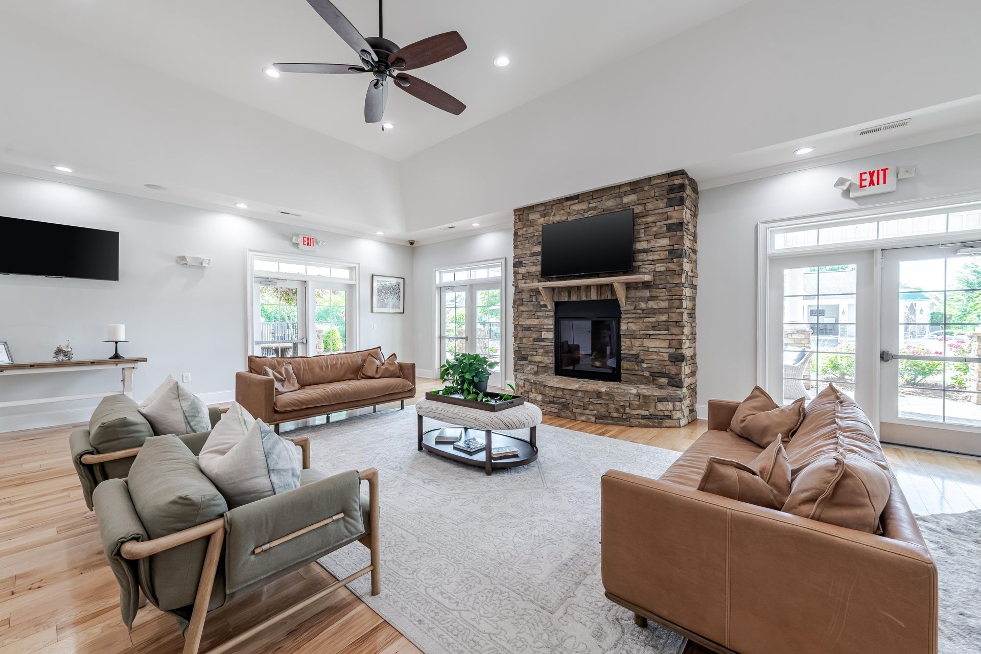 Lounge with a stone fireplace, brown leather sofas, and a rug. Sunlight streams through glass doors at Plantation at Pleasant Ridge in Greensboro, NC.