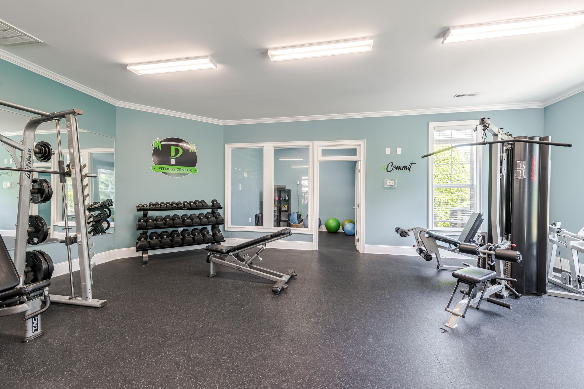 Gym with workout equipment on black rubber flooring, blue walls, and white trim at Plantation at Pleasant Ridge in Greensboro, NC.