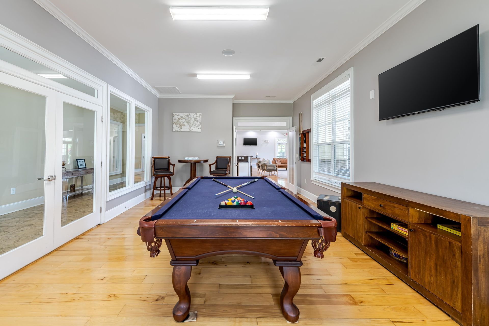 A pool table in a rec room with wood floors, blue felt, TV, and bar cabinet at Plantation at Pleasant Ridge in Greensboro, NC.