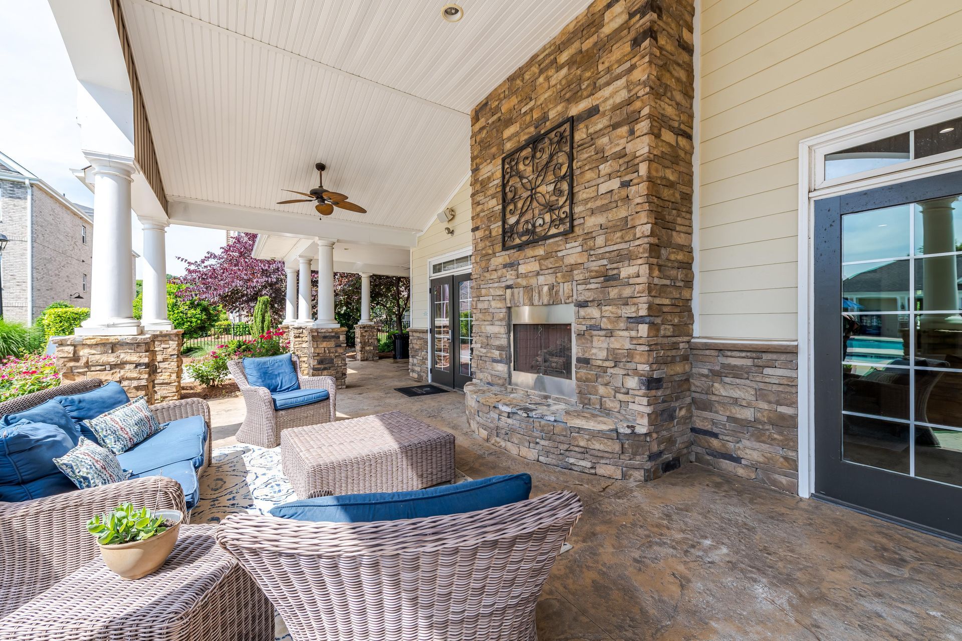 Covered patio with stone fireplace, wicker furniture, and blue cushions at Plantation at Pleasant Ridge in Greensboro, NC.