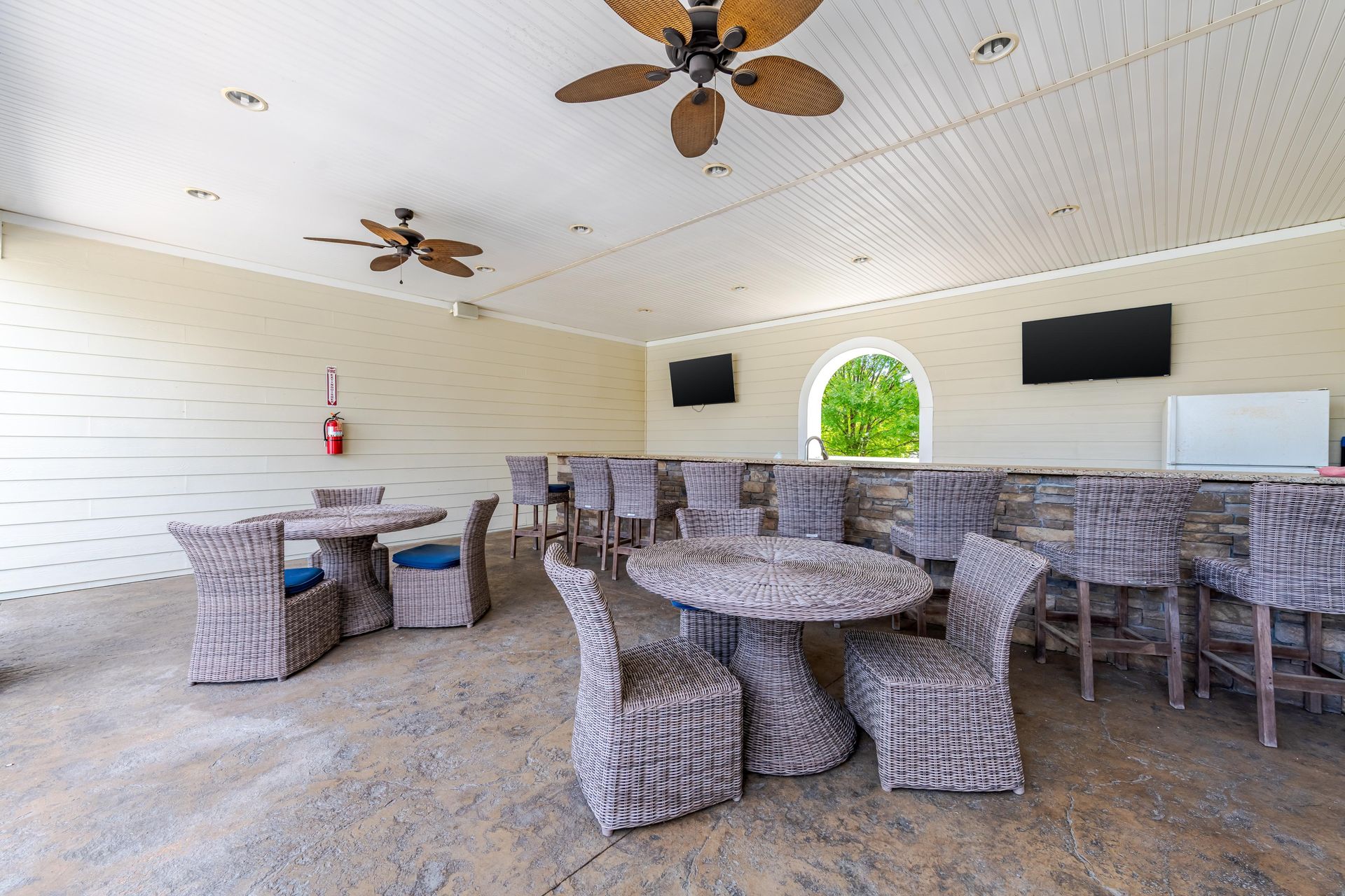 Outdoor covered seating area with tables, chairs, bar, and ceiling fans at Plantation at Pleasant Ridge in Greensboro, NC.