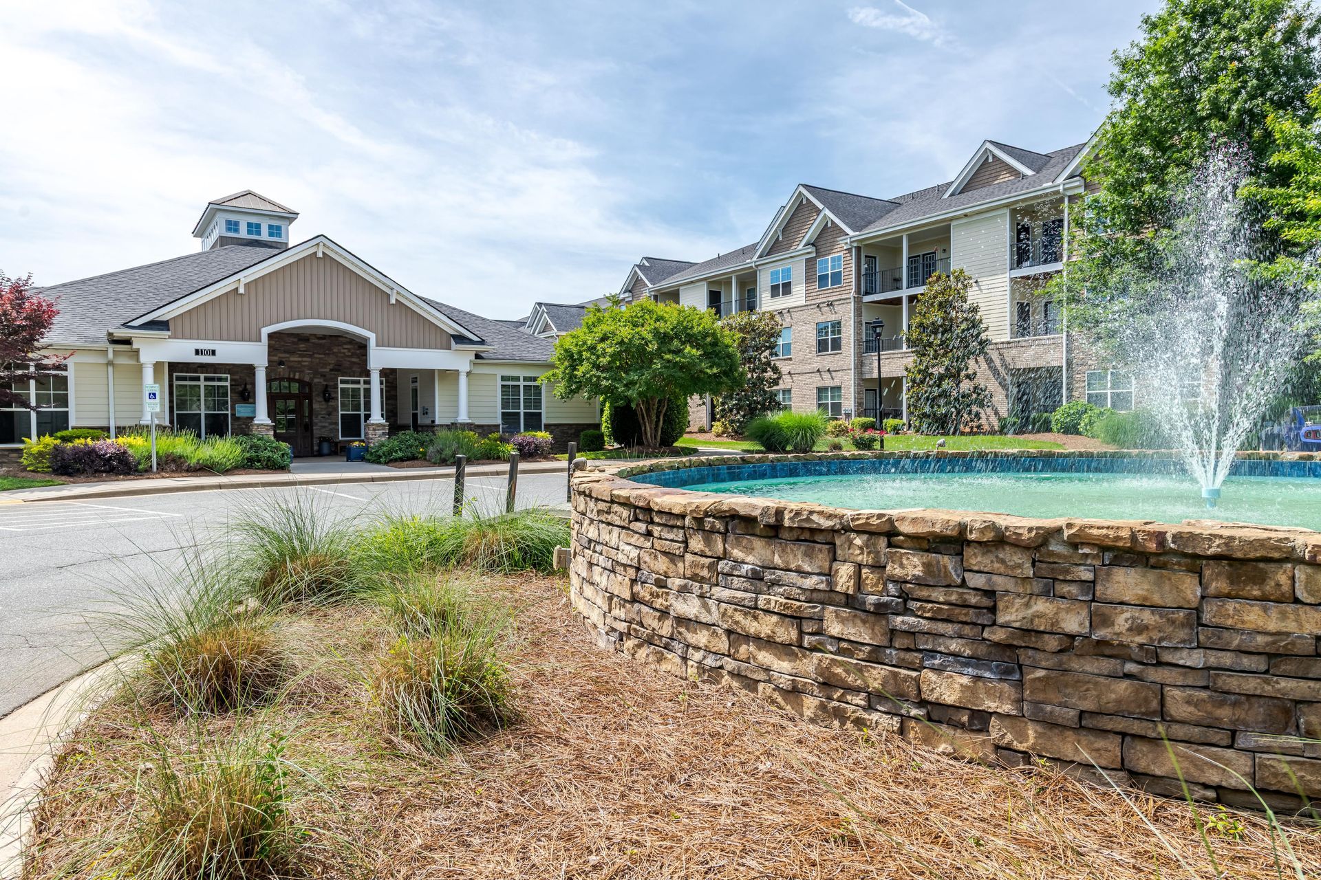 A senior living facility with a stone fountain in front at Plantation at Pleasant Ridge in Greensboro, NC.