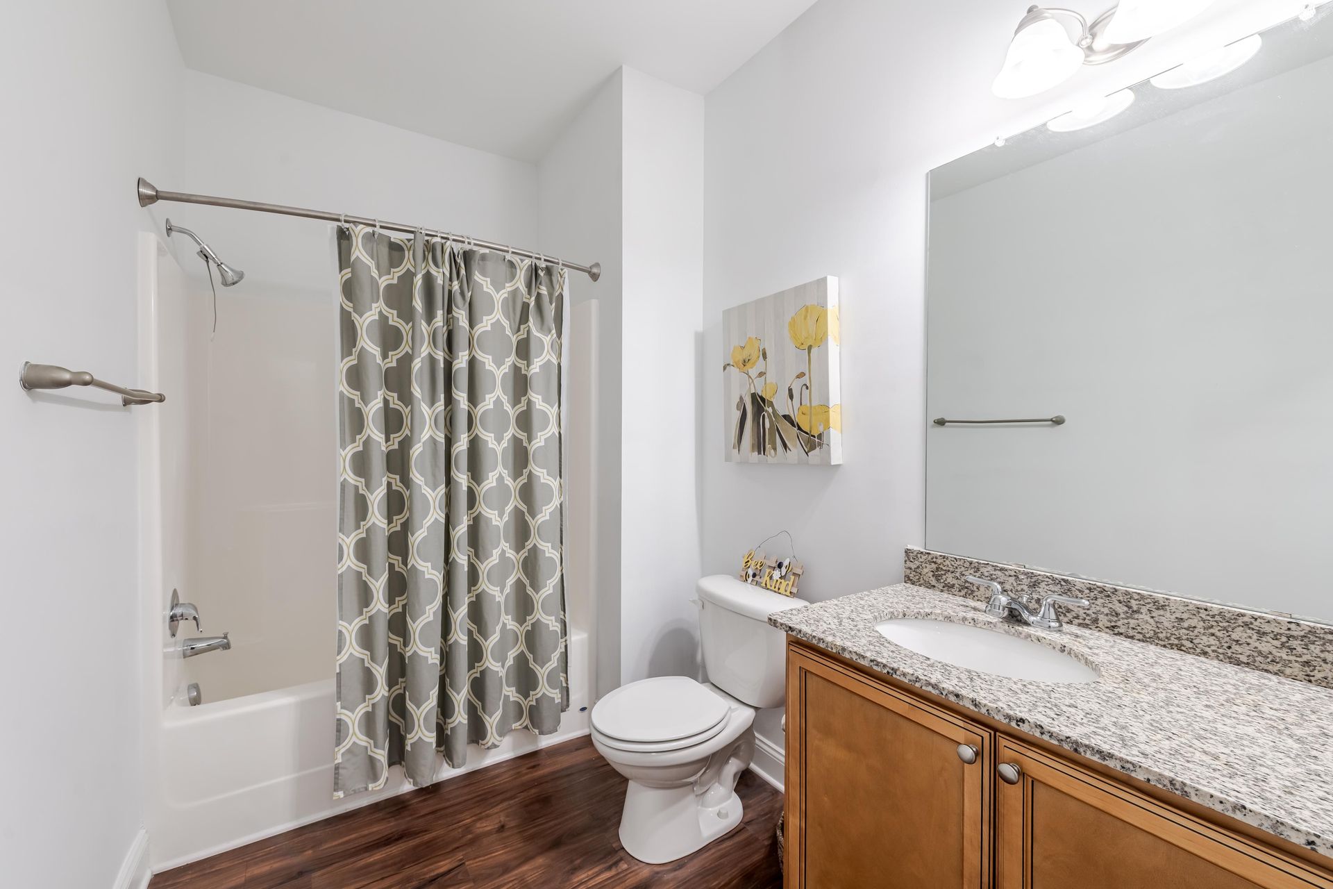 Bathroom with white walls, wood-look floor, gray and white shower curtain, vanity, and toilet at Plantation at Pleasant Ridge in Greensboro, NC.